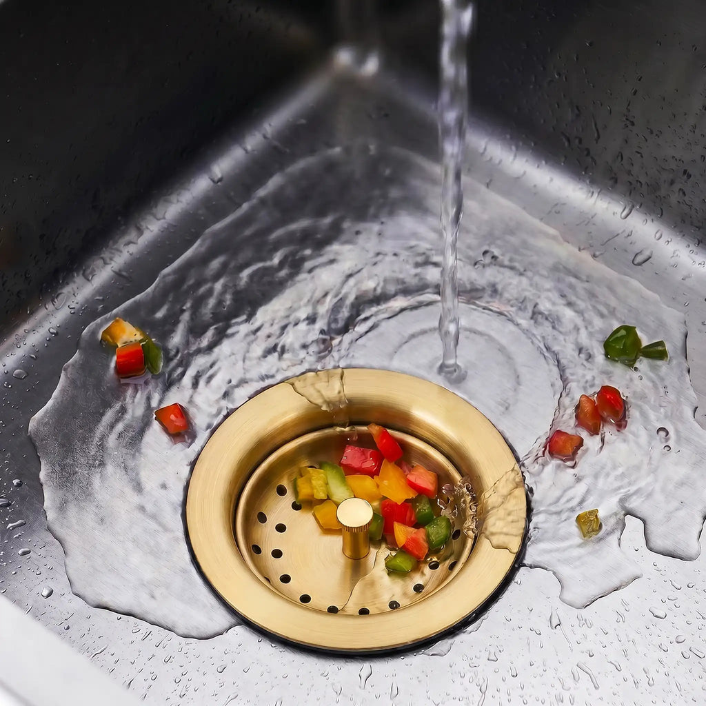 Gold kitchen sink strainer catching food scraps under running water