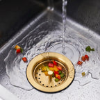 Gold kitchen sink strainer catching food scraps under running water